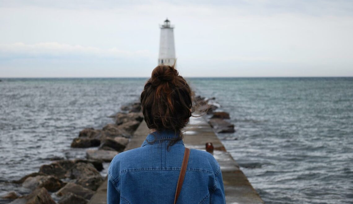 kobieta idąca w kierunku morskiej latarni